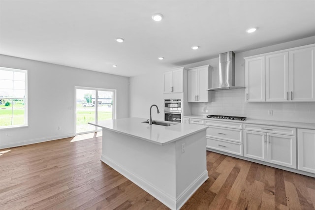 kitchen featuring sink, white cabinets, a kitchen island with sink, and wall chimney exhaust hood