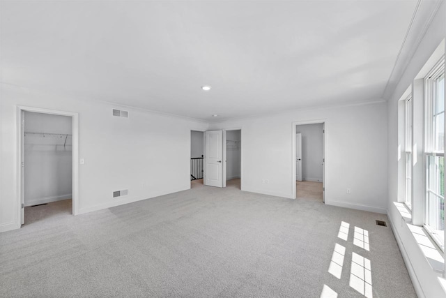 unfurnished bedroom featuring a walk in closet, ornamental molding, and light colored carpet