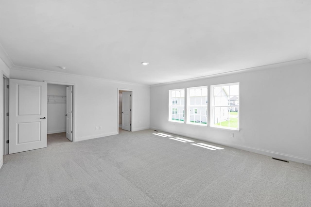 unfurnished bedroom featuring a walk in closet, a closet, crown molding, and light carpet