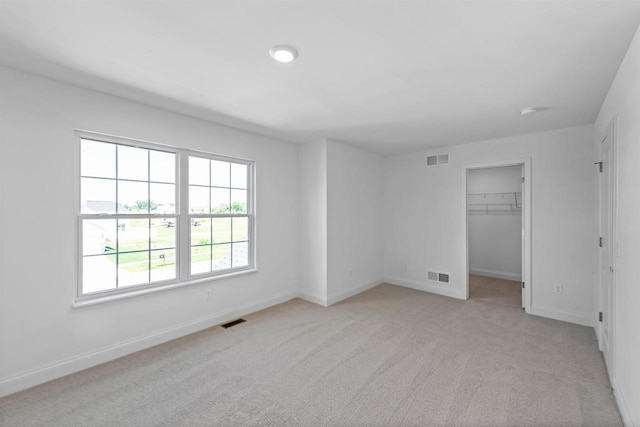 unfurnished bedroom featuring light colored carpet, a closet, and a spacious closet