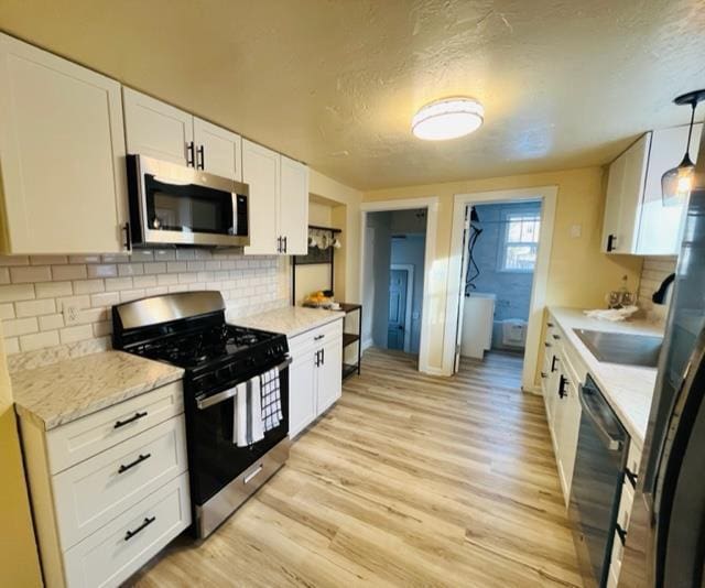 kitchen featuring pendant lighting, appliances with stainless steel finishes, white cabinetry, tasteful backsplash, and light hardwood / wood-style floors