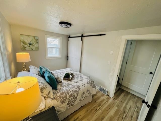 bedroom featuring a barn door, a textured ceiling, and light hardwood / wood-style floors