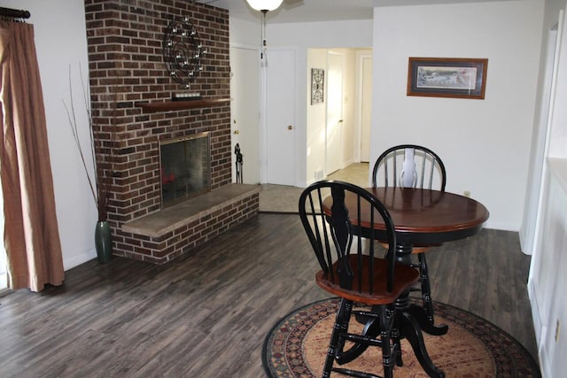 dining area featuring a brick fireplace and dark wood-type flooring