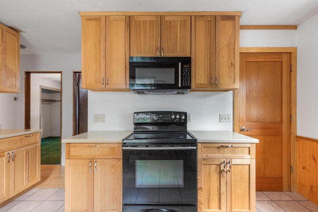 kitchen featuring light tile patterned floors, wood walls, and black appliances