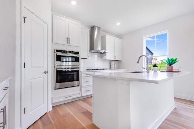 kitchen with sink, a center island with sink, white cabinetry, and wall chimney exhaust hood