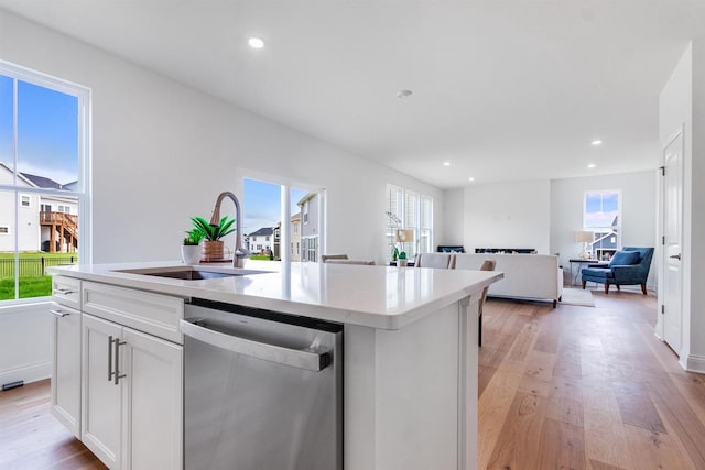 kitchen featuring sink, white cabinetry, dishwasher, light wood-type flooring, and an island with sink