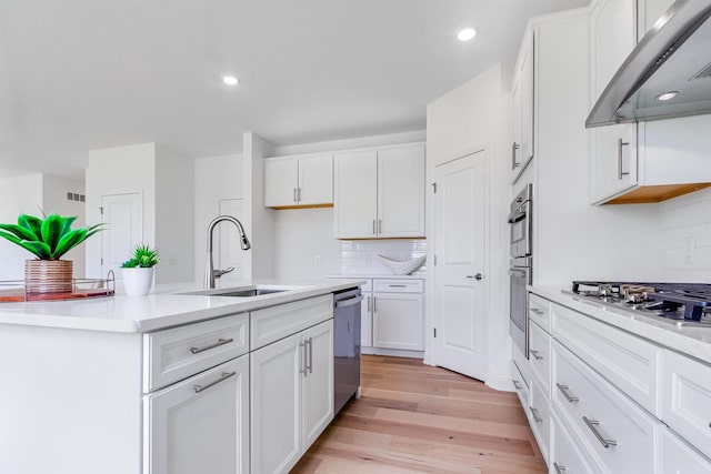 kitchen featuring sink, stainless steel appliances, white cabinetry, wall chimney exhaust hood, and light hardwood / wood-style flooring