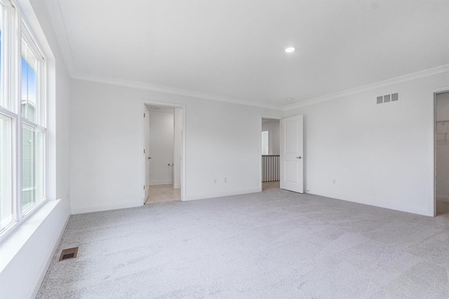 spare room with a healthy amount of sunlight, crown molding, and light colored carpet