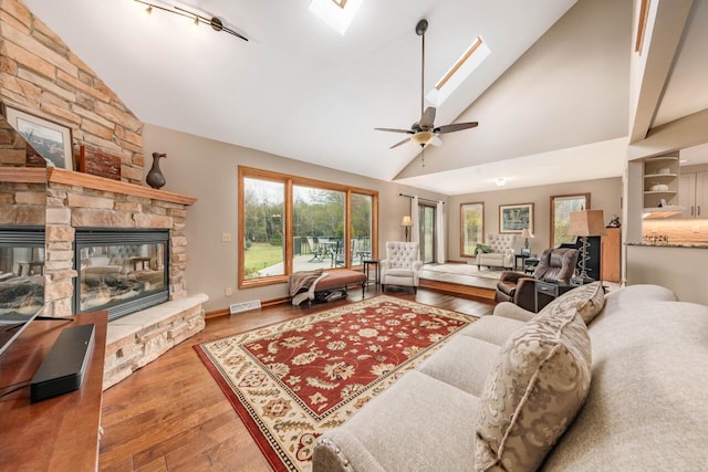 living room featuring ceiling fan, lofted ceiling with skylight, hardwood / wood-style floors, and a fireplace