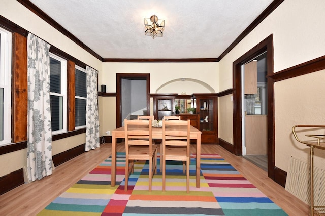 dining room with wood-type flooring, a textured ceiling, and ornamental molding