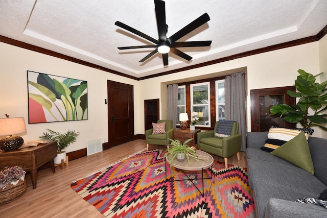 living room featuring light hardwood / wood-style floors, ceiling fan, a textured ceiling, and a tray ceiling