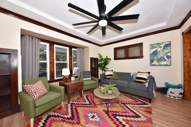 living room with a textured ceiling, ceiling fan, a tray ceiling, ornamental molding, and wood-type flooring