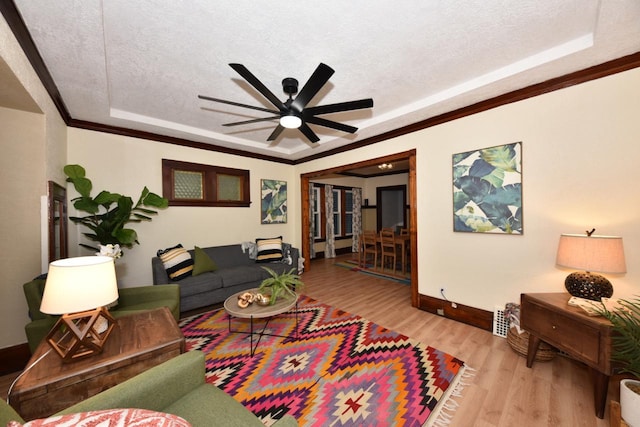 living room featuring a textured ceiling, ceiling fan, a tray ceiling, and light hardwood / wood-style flooring