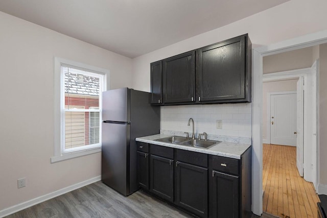 kitchen with light wood-type flooring, stainless steel fridge, tasteful backsplash, and sink