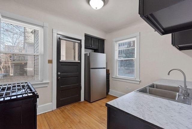 kitchen with sink, stainless steel refrigerator, ventilation hood, light wood-type flooring, and black range with gas stovetop