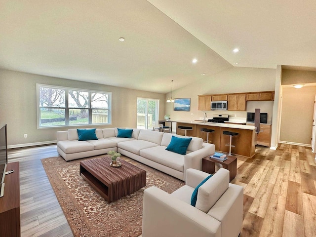 living room with lofted ceiling, sink, a chandelier, and light hardwood / wood-style flooring