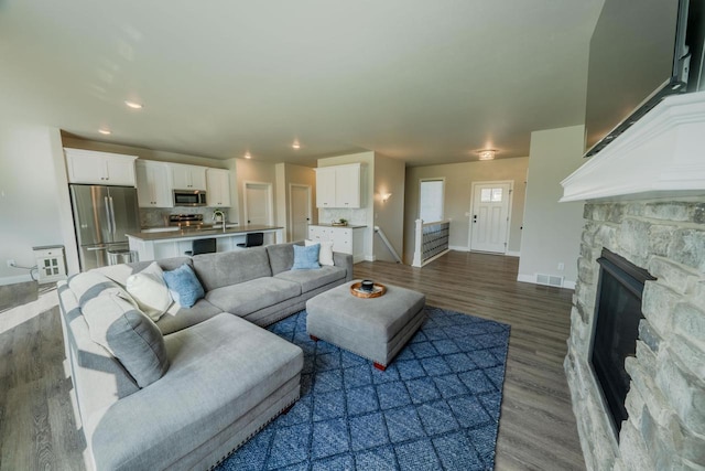 living room with hardwood / wood-style floors, sink, and a stone fireplace