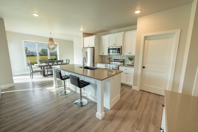 kitchen with decorative light fixtures, a center island with sink, white cabinets, and appliances with stainless steel finishes