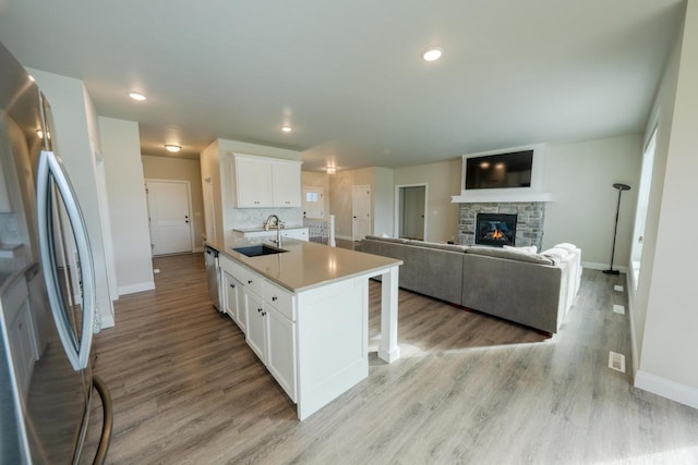 kitchen with stainless steel appliances, sink, white cabinetry, a fireplace, and an island with sink