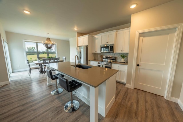 kitchen featuring pendant lighting, stainless steel appliances, a center island with sink, white cabinets, and sink