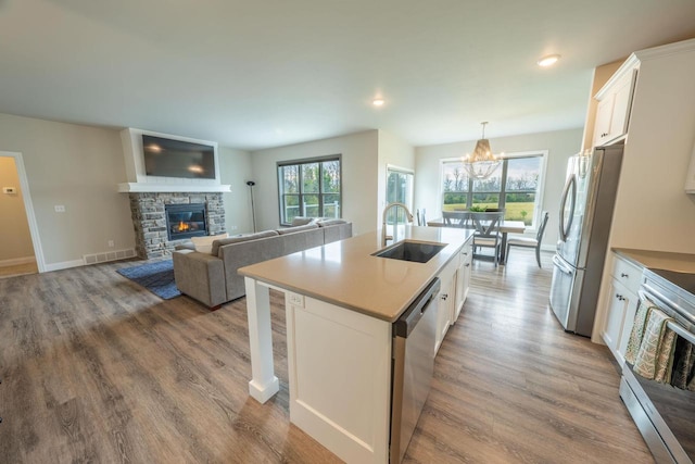 kitchen featuring sink, a center island with sink, a stone fireplace, and white cabinetry