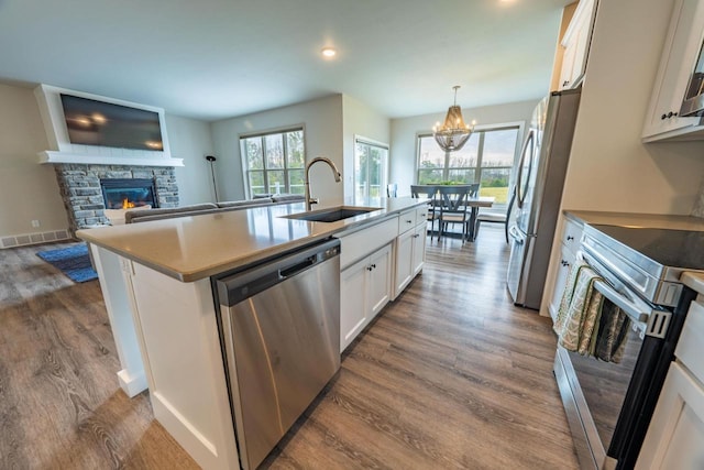 kitchen featuring a stone fireplace, appliances with stainless steel finishes, an island with sink, sink, and white cabinetry