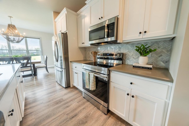 kitchen featuring a chandelier, pendant lighting, tasteful backsplash, white cabinets, and appliances with stainless steel finishes