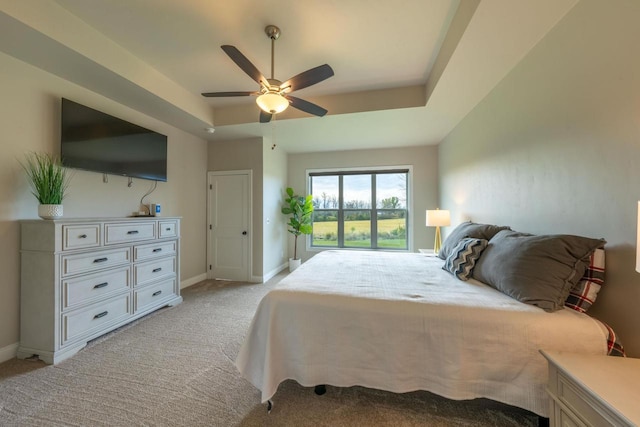 bedroom with a raised ceiling, ceiling fan, and light colored carpet