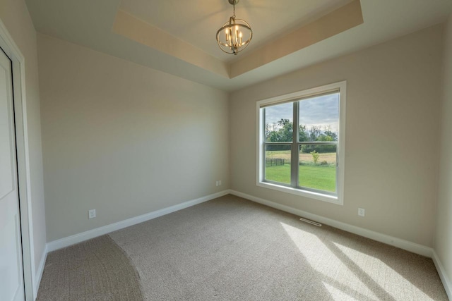 empty room with carpet floors, a tray ceiling, and a chandelier