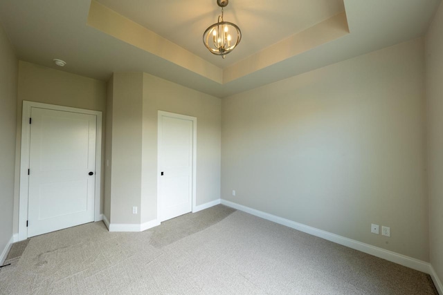 unfurnished bedroom with light colored carpet, a raised ceiling, and a chandelier