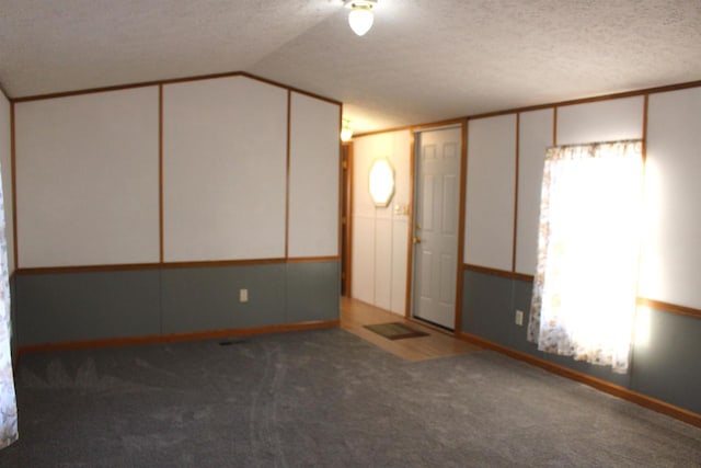 unfurnished room with a textured ceiling, vaulted ceiling, and carpet flooring