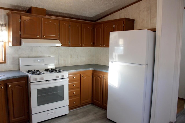 kitchen featuring a textured ceiling, vaulted ceiling, white appliances, hardwood / wood-style flooring, and decorative backsplash