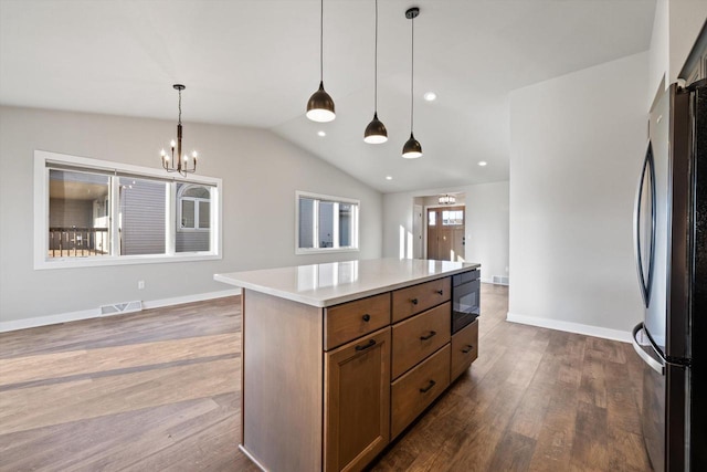 kitchen with decorative light fixtures, vaulted ceiling, black fridge, a kitchen island, and a notable chandelier