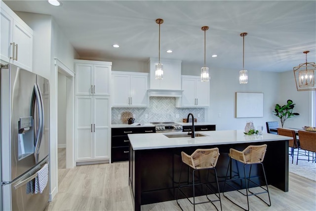 kitchen featuring hanging light fixtures, stainless steel appliances, a kitchen island with sink, white cabinets, and sink