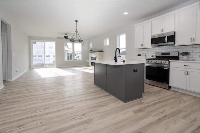 kitchen with decorative light fixtures, white cabinets, stainless steel appliances, a center island with sink, and light hardwood / wood-style flooring