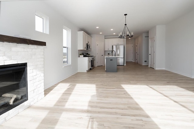 kitchen featuring pendant lighting, white cabinets, stainless steel appliances, a brick fireplace, and a center island with sink