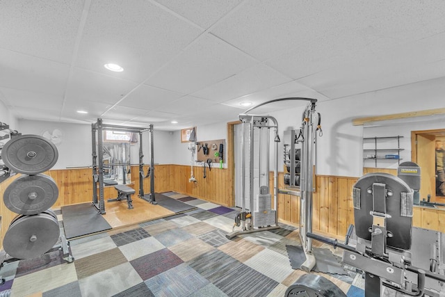 workout room featuring a paneled ceiling and wooden walls