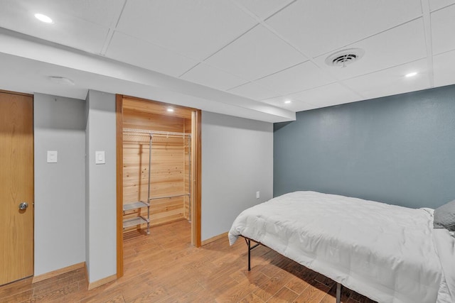 bedroom with a drop ceiling, a closet, and hardwood / wood-style floors