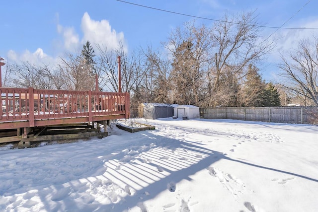 yard covered in snow with a storage unit and a wooden deck