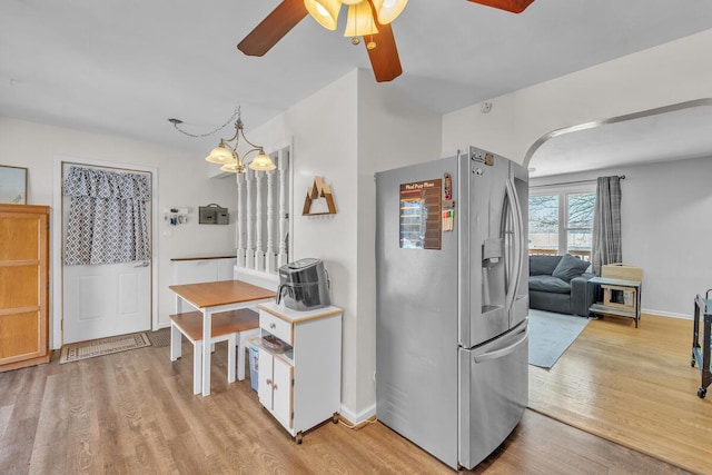 kitchen with white cabinets, light wood-type flooring, ceiling fan with notable chandelier, stainless steel fridge, and pendant lighting