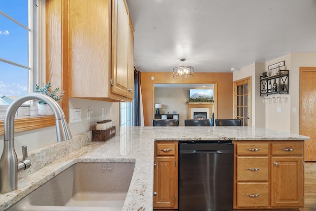 kitchen featuring sink, black dishwasher, hanging light fixtures, light stone countertops, and a notable chandelier