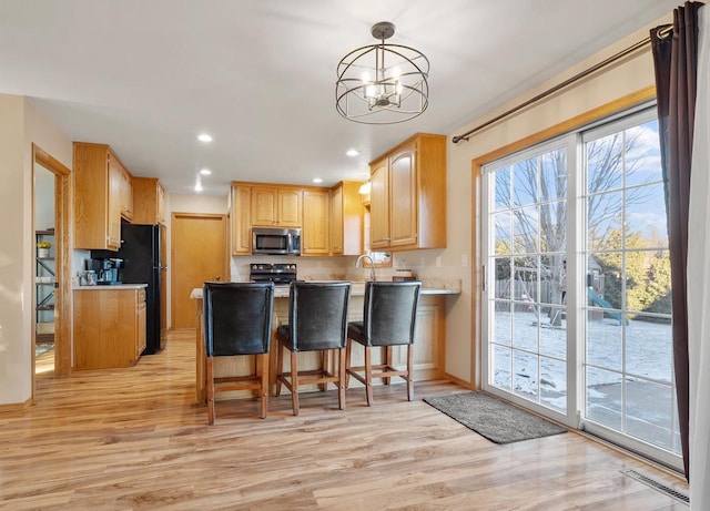 kitchen featuring light wood-type flooring, a breakfast bar area, electric range, a chandelier, and pendant lighting