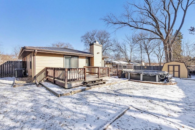 snow covered rear of property featuring a swimming pool side deck, central air condition unit, and a storage unit