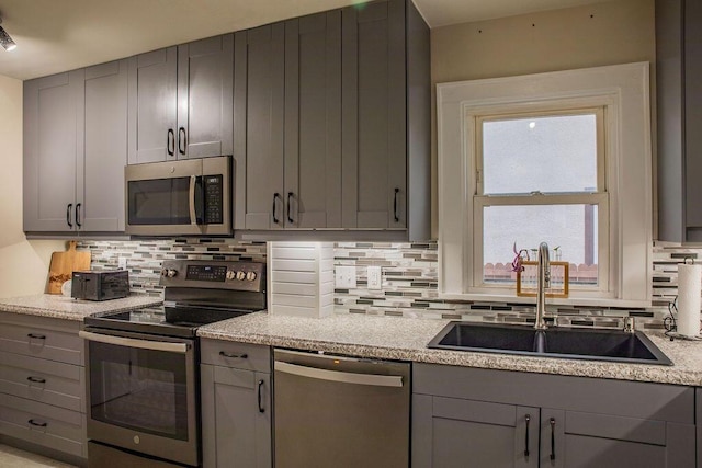 kitchen featuring gray cabinetry, stainless steel appliances, light stone counters, decorative backsplash, and sink