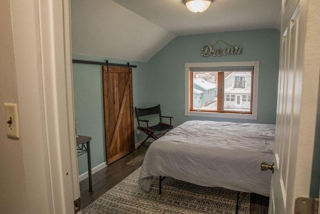 bedroom featuring dark hardwood / wood-style flooring, vaulted ceiling, and a barn door