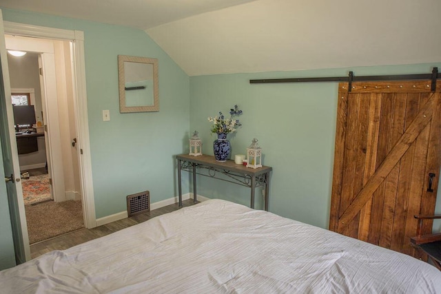 bedroom featuring vaulted ceiling, a barn door, and light hardwood / wood-style flooring