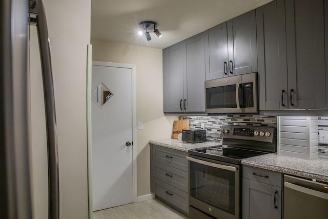 kitchen with light stone counters, appliances with stainless steel finishes, gray cabinets, and decorative backsplash