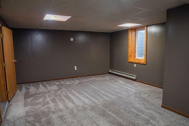 basement featuring a paneled ceiling, light carpet, and a baseboard heating unit