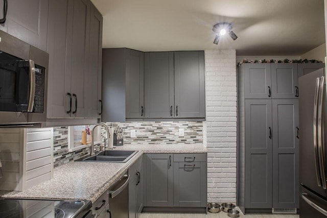 kitchen featuring stainless steel appliances, sink, light stone counters, backsplash, and gray cabinetry