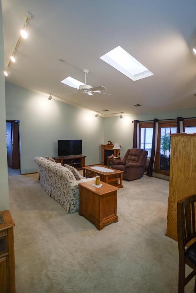 living room with rail lighting, ceiling fan, vaulted ceiling with skylight, and light colored carpet